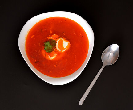 A plate of freshly cooked borscht with sour cream and a tablespoon on a black background.