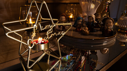 Christmas decoration with golden star candle holder and “Merry Christmas” text, glowing candles, and Nativity figurines creating a warm and festive holiday atmosphere.