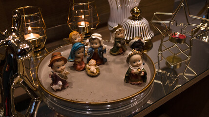 Nativity scene with baby Jesus, Mary, Joseph, and the Wise Men surrounded by golden Christmas decor, candles, and a star-shaped candleholder. Warm festive holiday atmosphere.