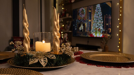 Elegant Christmas table centerpiece with golden candles, wreath and glowing candlelight. Cozy festive dinner decoration with warm holiday atmosphere, perfect for seasonal celebrations.