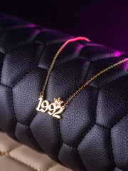 Close-up of a metallic gold pendant in the shape of "1992" on a chain, on a black leather background