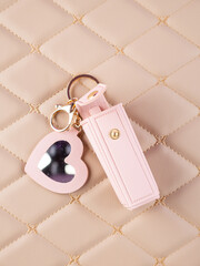 Close-up of a pink leather lipstick case with a heart-shaped mirror, elegantly placed on a  beige background