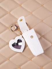 Close-up of a white leather lipstick case with a heart-shaped mirror, elegantly placed on a  beige background