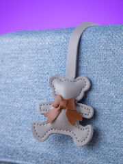 Close-up of a gray leather bag charm in the shape of a cute bear on a  blue bag