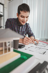 Young male architect working at office desk, drawing construction plans and using drafting tools, focused on building design while showing creativity and dedication in architecture.