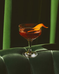 Red cocktail in elegant coupe glass with orange peel garnish on green velvet