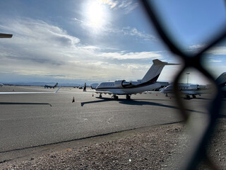 airplane at the airport through a chain link fence - general aviation airfield with jet planes on the tarmac