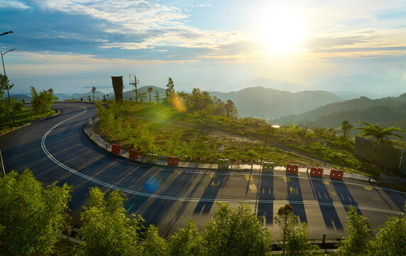 Winding mountain road at sunrise illuminating lush green landscape