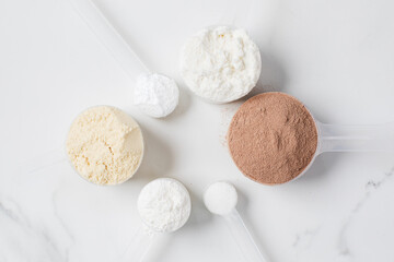 Assorted protein powder and supplement scoops on white marble background for nutrition and fitness