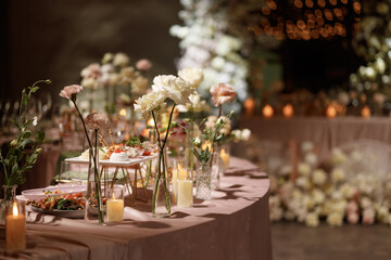 Wedding banquet table decorated with flowers, candles and food in festive hall with dark background. Concept of celebration, romance, event decoration, reception.