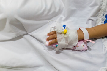 Little girl's hand with intravenous or IV line and hospital patient bracelet attached in hospital bed