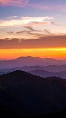 Fototapeta premium Mountain range at sunset, layers of hills fade into a vibrant orange and purple sky