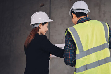 Construction manager and engineer dressed in orange work vests and hard helmets explore...