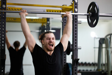 Fototapeta premium Young man intense effort during overhead press in gym