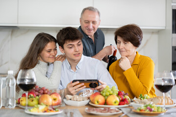 Happy bonding family looking at cellphone screen, laughing at funny video or photos in social networks, having fun at home