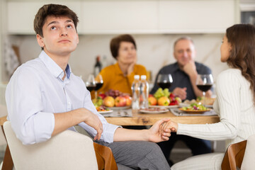 Dissatisfied guy turned away from the festive table, where his family and friends were having a conversation. Quarrel during home dinner