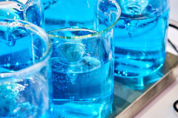 Clear blue liquid swirling in laboratory beakers filled with bubbles and reflecting light