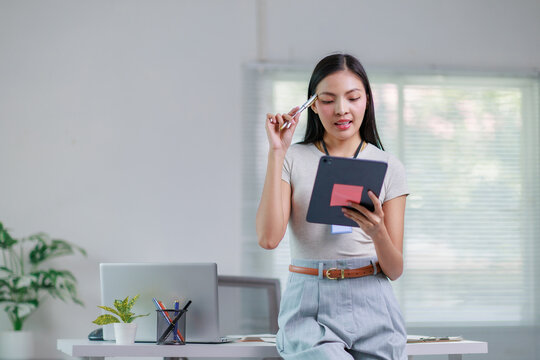 Young Asian businesswoman using a digital tablet while contemplating her work in a sleek, modern office environment