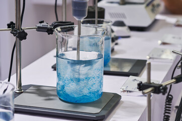 Laboratory equipment mixing clear blue liquid in a beaker on a hot plate