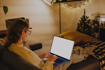 A young woman sitting comfortably on a couch using a laptop during a cozy and festive evening at...