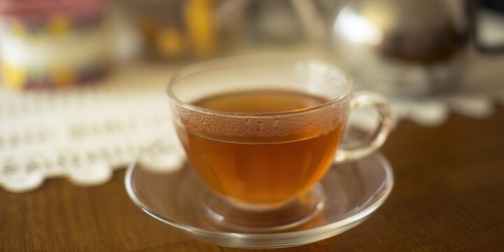 A clear teacup filled with tea sits on a saucer, inviting relaxation and warmth.