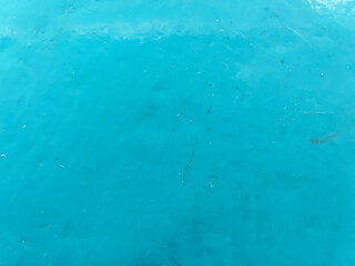 A vibrant, textured macro shot of a bright turquoise blue plastic surface with visible scratches, scuff marks, and dust, suggesting a well-used object like a bucket or a container.