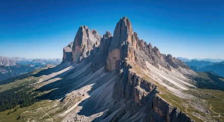 Jagged, rocky mountain peaks rise above forested foothills under a clear blue sky