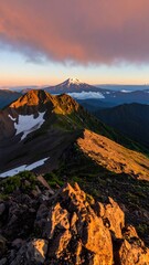 Mountain vista at dawn.  Sunrise hues paint jagged peaks, snow-capped summit, and shadowed slopes.  Rocky terrain, lush green slopes, and clouds