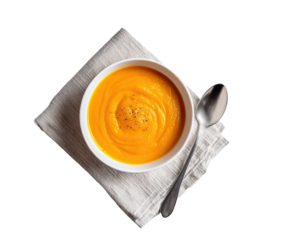 Creamy, orange soup in a white bowl, topped with seasoning, sits on a linen napkin.  A spoon rests beside it