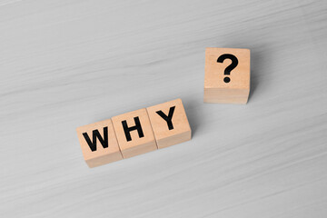 WHY and question mark held by finger on wooden block