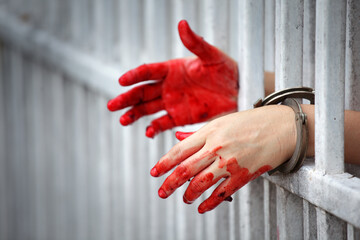 Hands with Red Paint Behind Jail Bars Symbolizing Guilt and Crime