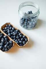 Fresh blueberries in small craft cartons and glass jar on white table
