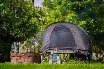 Camping tent and gas lantern on the grass next to a wood stove in the forest.