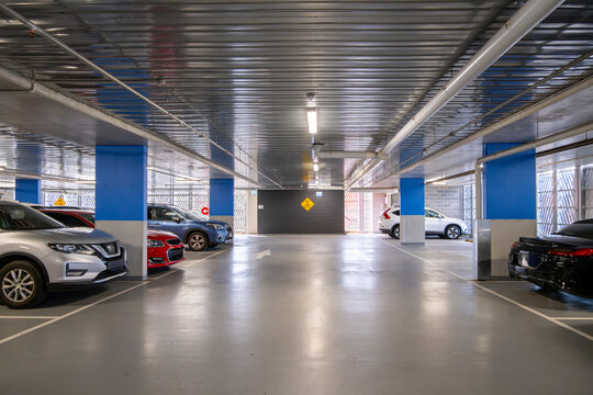 Indoor covered car park with parked vehicles and structural columns within a multi-level facility. Modern urban parking infrastructure with ventilation