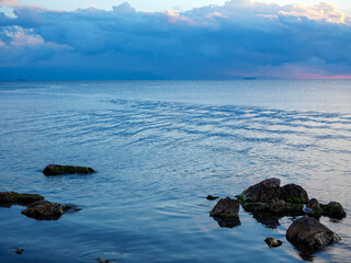 A tranquil evening seascape with several rocks silhouetted in the calm sea and a distant island under a softly colored sky a minimalist and peaceful view
