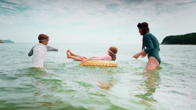 Active mother holds daughter legs while playing in water sea with siblings. Genuine happiness and connection highlight family bonding, parenting and summer playtime on beach.