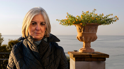 Mature Woman Outdoors By Flower Planter Overlooking a Serene Ocean View
