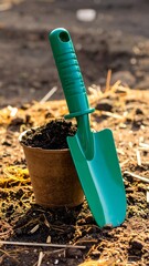 Small green trowel beside a pot of dark soil on garden ground