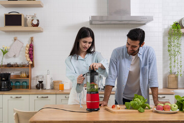 Couple blending fresh fruits and vegetables in kitchen preparing smoothie for healthy lifestyle together
