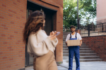 Courier delivering package to woman using smartphone