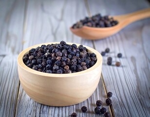 Wooden bowl of black peppercorns on a weathered wood table