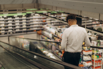 Man Riding Escalator in Supermarket With Shelves Filled with Products