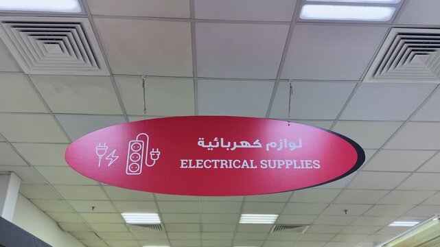 Close-up of electrical supplies section sign in a retail hardware store, showing Arabic and English text. Perfect for themes of shopping, retail, or multicultural business.