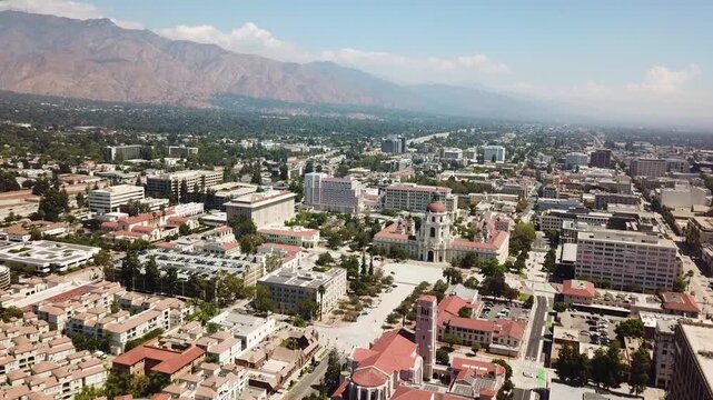 Drone aerial of Pasadena, California, focusing on Pasadena City Hall, with surrounding urban streets, neighborhoods, and the San Gabriel Mountains in the distance.