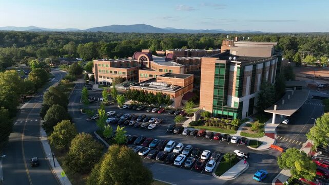 Parking cars on parking area of American hospitals building at sunset time. Aerial top down. Traffic on street in suburb. Centra Lynchburg General Hospital In USA.