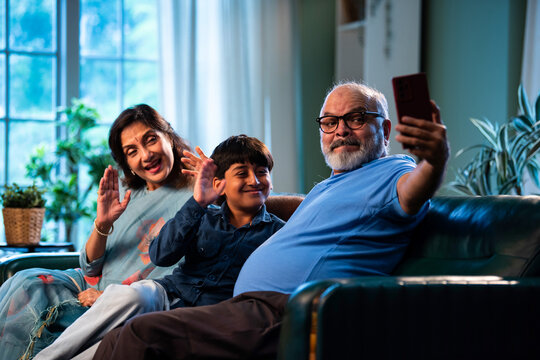 Indian grandparents with grandchild using smartphone for video call while sitting indoors