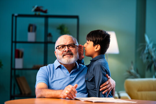Indian boy shares gossip secretly with grandfather at home sitting at table