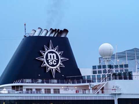 The black funnel of a large white MSC cruise ship showing the company's star logo and a radar dome against a pale sky