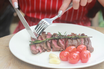 A steak on a white plate ready to eat, garnished with red tomatoes and rosemary for flavor.