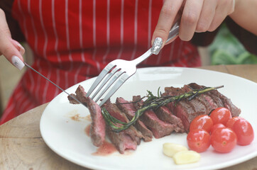 A steak on a white plate ready to eat, garnished with red tomatoes and rosemary for flavor.